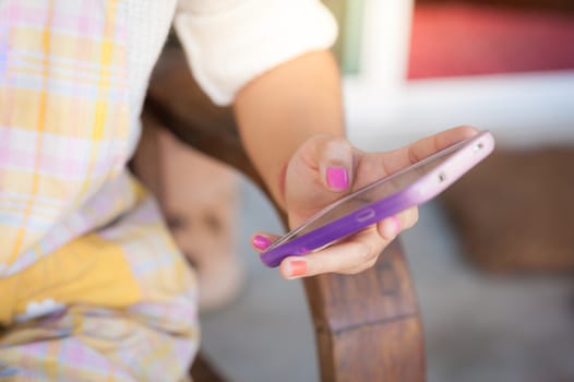 Young hipster woman holding smartphone on her left hand while sitting on wood bench in morning time