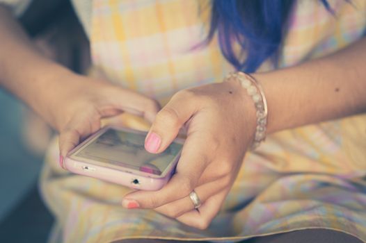 Young hipster woman using smartphone while sitting on wood bench in morning time with vintage filter effect