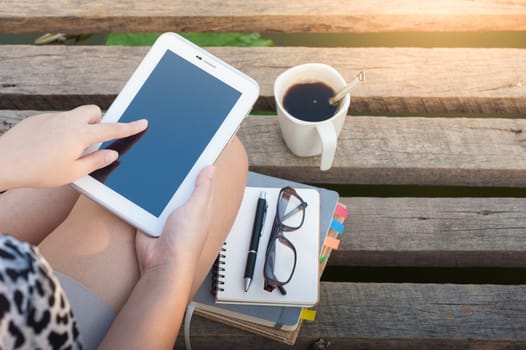 Young woman touching on small talet screen while sitting on wood bridge in morning time on weekend