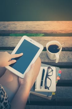 Young woman touching on small talet screen while sitting on wood bridge in morning time on weekend with vintage filter effect