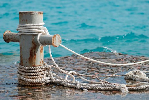 Rusty mooring bollard with ship ropes and  clear turquouse sea ocen water on background.