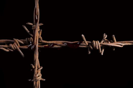 Rusty barb wire cross isolated on black background. Religious wars. 