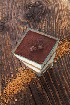 Tiramisu dessert with coffee beans and instant coffee on wooden textured table. Traditional tiramisu dessert, rustic, country style.