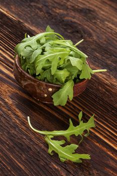 Fresh arugula salad in wooden bowl on wooden table. Healthy green salad eating. 