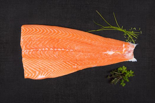 Fresh raw salmon background. Salmon steak with fresh herbs on black background, flat lay.