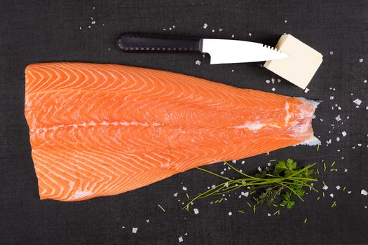 Fresh raw salmon background. Salmon steak with fresh herbs on black background, flat lay.