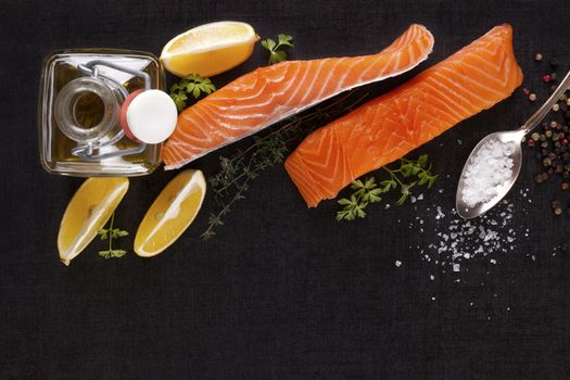 Salmon background with copyspace. Salmon steak, lemon, rosemary and parsley leaf and salt on black background, flat lay.