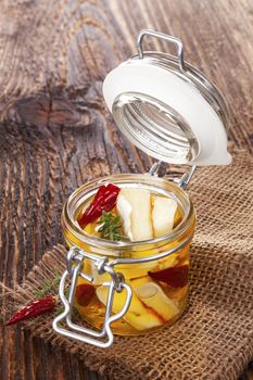 Marinated cheese in glass jar on brown wooden background. Culinary marinated cheese, rustic styles.