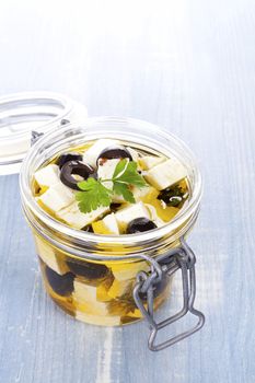 Marinated greek feta cheese in glass jar on blue wooden background. Culinary marinated cheese, rustic styles.