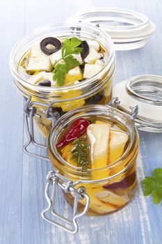 Marinated cheese in glass jar on blue wooden background. Culinary cheese eating. 