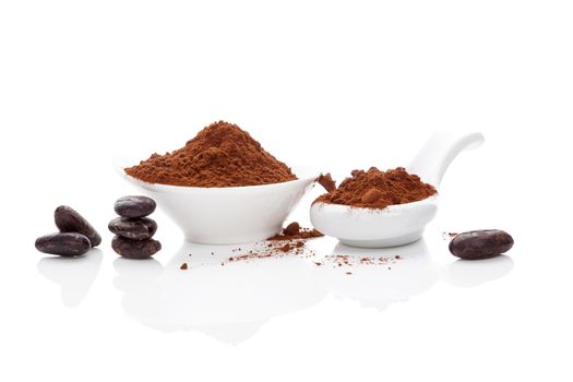 Cocoa beans and cocoa powder in white bowl and white spoon on white background. Healthy superfood.