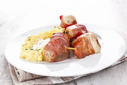 Delicious poultry and bacon kebab with mashed potatoes on white plate. Culinary meat rolls on skewer. 