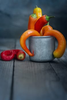 A beam of multi-colored chili in a Cup on the table out of old rough boards, and a gray background. Rustic style, defocused background.