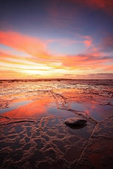 Vertical views across the vast rockshelf of Long Reef at low tide during a vivid sunrise with reflections of the sky in the wet rocks exposed. Lone fisherman at horizon gives dimension to space. Orientation suitable for magazine or vertical brochure.