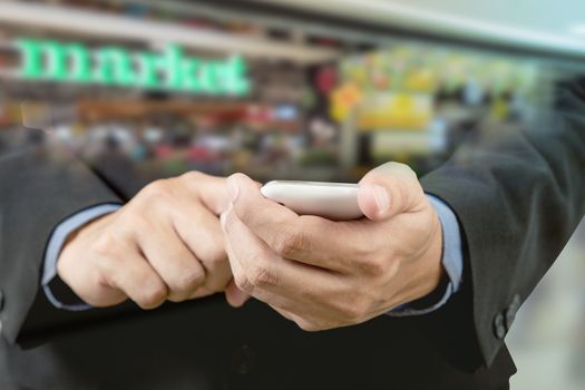 Businessman touch smart phone in hand with blur background of shopping mall market