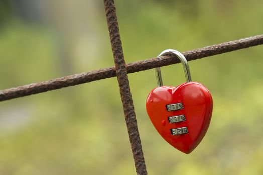 Red padlock in the shape of a heart fixed to a rusted concrete wire construction
