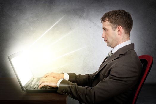 Focused businessman working at laptop sitting on chair at table. Concept of Internet business. Monitor of laptop shine rays of light