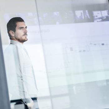 Business man making a presentation in front of whiteboard. Business executive delivering a presentation to his colleagues during meeting or in-house business training. View through glass.