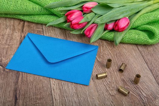 Blue envelope, tulips and bullets on a wooden background