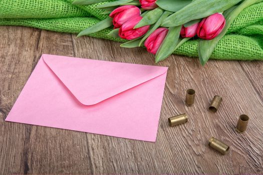 Pink envelope, tulips and bullets on a wooden background
