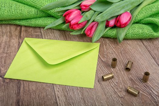 Green envelope, tulips and bullets on a wooden background