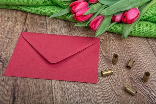 Red envelope, tulips and bullets on a wooden background