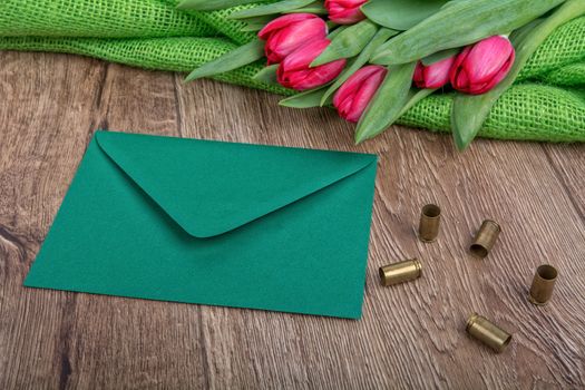 Green envelope, tulips and bullets on a wooden background