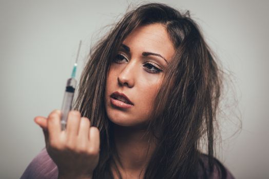 Portrait of a beautiful girl drug addiction. She is holding syringe with drugs.