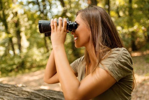 Beautiful young woman walking through forest and exploring thru binoculars.
