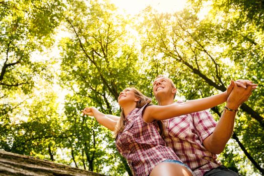 Beautiful young couple sitting on fallen tree in the forest and enjoying. 