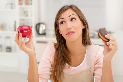 Beautiful young woman in the kitchen decision between apple or sweet chocolate cake.