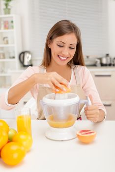 Beautiful young woman in the kitchen squeezing orange juice with an electric juicer.