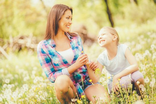 Happy cute little girl blowing dandelion with mother in the park.