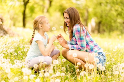 Happy cute little girl blowing dandelion with mother in the park.