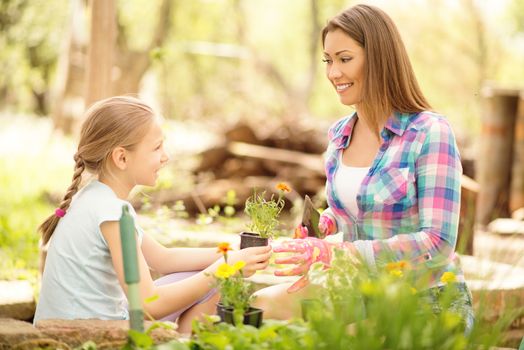 Cute little girl assisting her mother planting flowers in a backyard.