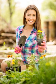 Portrait of a smiling young woman planting flowers in the garden. Looking at camera.