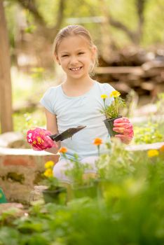 Portrait of a smiling little girl planting flowers in the garden. Looking at camera.