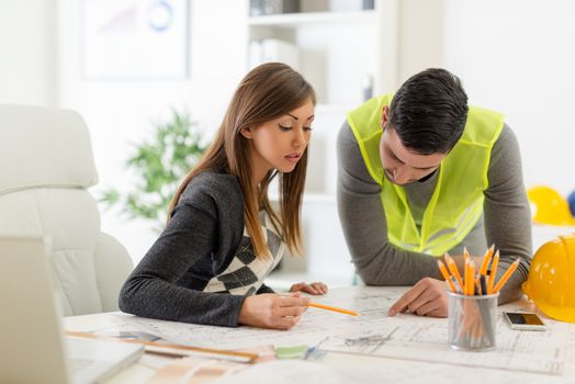 Two young architects checking the construction plans in office.