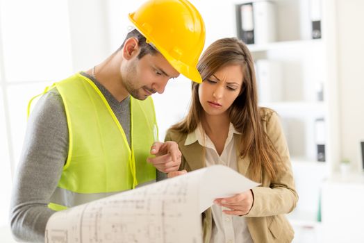 Two young architects discussing construction plans in office.