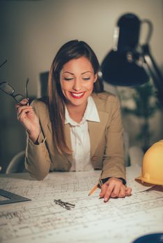 Young smiling female architect analyzing blueprint in the office.
