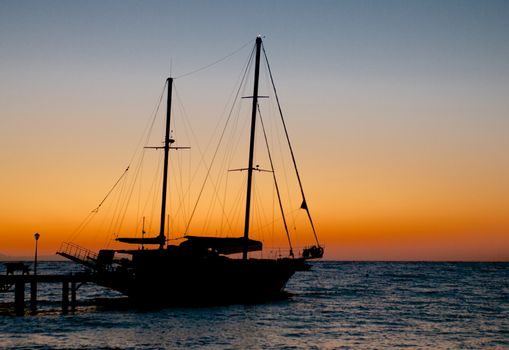 Seascape with Small Sailing Ship and Pier Early Morning on Sunrise Sky background Outdoors