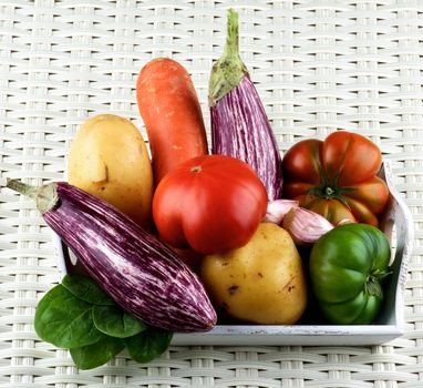Arrangement of Fresh Raw Vegetables with Striped Eggplants, Green and Red Tomatoes, Potato, Carrot and Garlic on Wooden Tray closeup on Wicker background