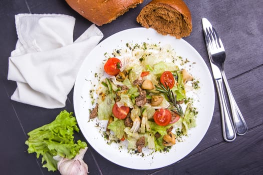 Concept: healthy food. Homemade salad with beef mushrooms and vegetables on white plate with ingredients bread and cutlery around