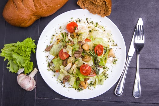 Concept: healthy food. Homemade salad with beef mushrooms and vegetables on white plate with ingredients bread and cutlery around