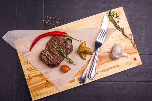 Concept: healthy food. Homemade grilled veal steak and vegetables on a wooden board with ingredients and cutlery around