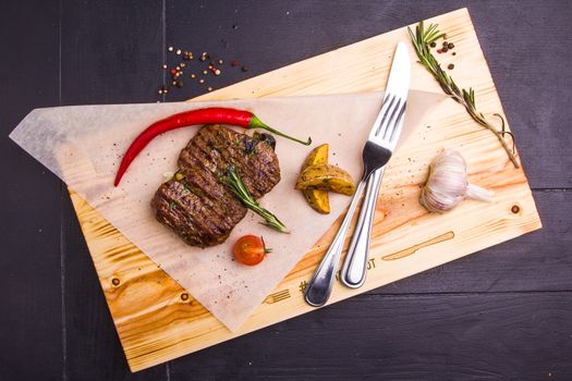 Concept: healthy food. Homemade grilled veal steak and vegetables on a wooden board with ingredients and cutlery around