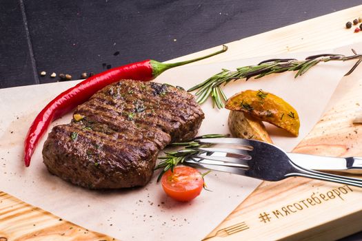 Concept: healthy food. Homemade grilled veal steak and vegetables on a wooden board with ingredients and cutlery around