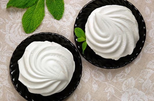 White sweet marshmallow dessert on black saucers with sprigs of fresh mint on linen fabric.