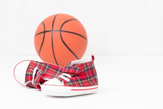 Pair of baby sized athletic shoes in front of a basketball.