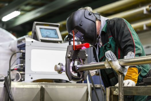 Industrial operator setting  computer controlled process of orbital welding machine in inox pipes manufacturing workshop.